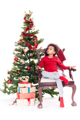Portrait of cute mixed race little boy sitting in chair near Christmas tree