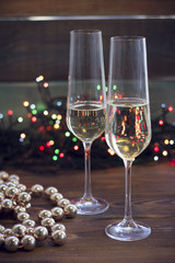 Two glasses of champagne and gold beads on a table.Dark colored wooden background. Christmas fairy lights on the back. Dark colorful bokeh