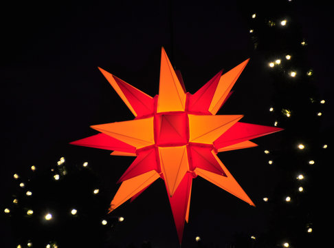 Orange-roter Weihnachtsstern leuchtend vor tiefschwarzem Himmel mit Lichterkette