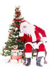 Portrait of Santa Claus sleeping in chair next to Christmas tree, heap of gift boxes near him