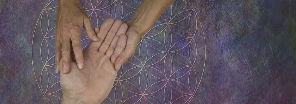 Your Palms are a map of your past and future life - female palm reader holding a male hand examining the lines and bumps against a flower of life rustic stone background
