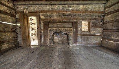 Fototapeta premium Pioneer Log Cabin Interior. Wooden interior of historic pioneer cabin living room with hardwood floor and fireplace.