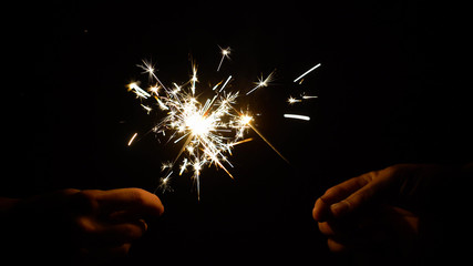 hands holding burning sparklers or bengal lights