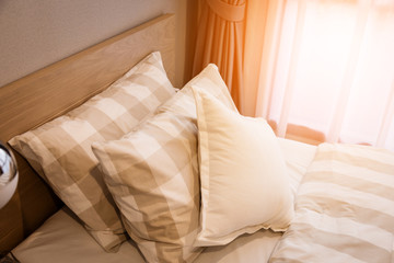 contemporary interior decoration with clean white pillows and bed sheets in bedroom. Close-up. Lens flair in sunlight.