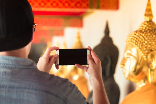 Tourist man holding a smart phone and take picture of a golden buddha in famous temple in Asia. Wat Pho in Bangkok, Thailand