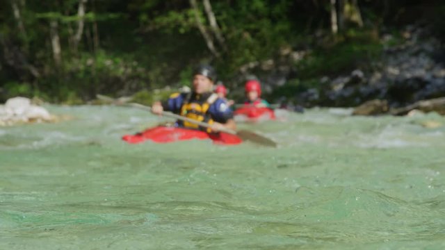 SLOW MOTION DOF: Group of kayakers gliding on emerald green river on sunny day. People kayaking down a stunning crystal-clear river in summer. Tourists enjoying their vacation on kayaking adventure.