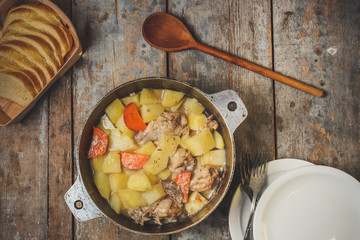 chicken meat stewed with potatoes, carrots and spices in a cast-iron pot on a wooden background