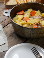 chicken meat stewed with potatoes, carrots and spices in a cast-iron pot on a wooden background
