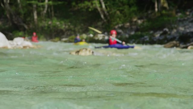 SLOW MOTION DOF: Group of kayakers gliding on emerald green river on sunny day. People kayaking down a stunning crystal-clear river in summer. Tourists enjoying their vacation on kayaking adventure.