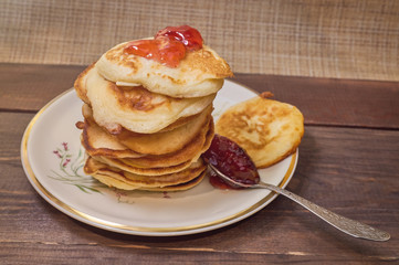 A pile of pancakes with jam and a spoon on a wooden background