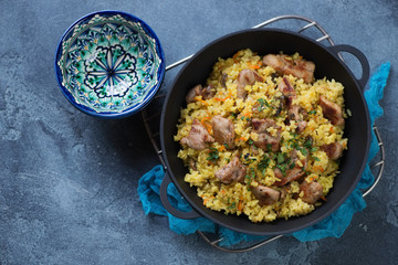 Cast-iron pan with pilaf on a metal cooling rack and pialas, top view on a blue stone background
