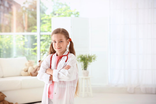 Adorable little girl in white doctor's coat with stethoscope at home