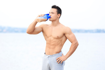 Handsome young man drinking protein shake on river bank