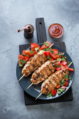 Plate with chicken lula kebabs and fresh vegetables on a black wooden serving board, gray concrete background, vertical shot