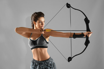 Sporty young woman practicing archery on grey background