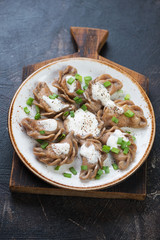 Boiled vareniki or dumplings stuffed with sauerkraut and served with sour cream and green onion, studio shot, selective focus