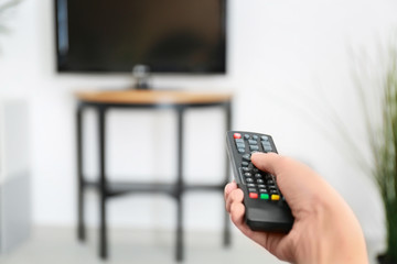 Woman with TV remote control switching channels, closeup