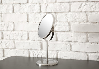 Small mirror on table near brick wall