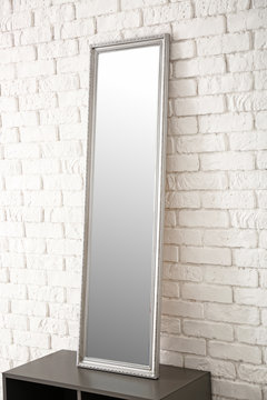 Modern mirror on stand near brick wall