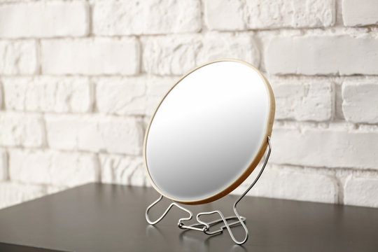 Small mirror on table near brick wall