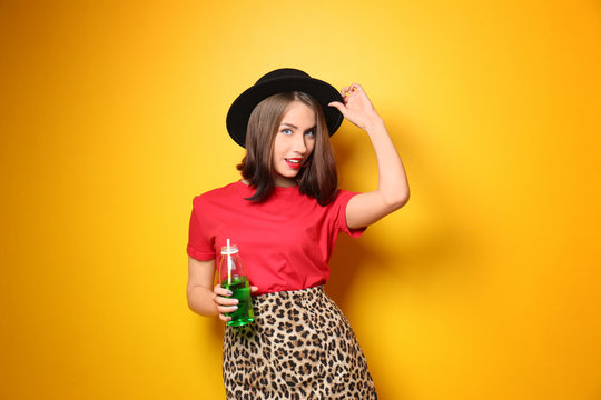 Attractive hipster girl with drink on color background