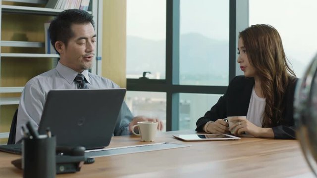 two asian corporate executives meeting in office discussing business using digital tablet