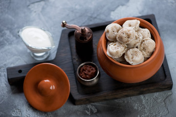 Ceramic pot with boiled meat dumplings or pelmeni on a black wooden serving tray, studio shot, selective focus
