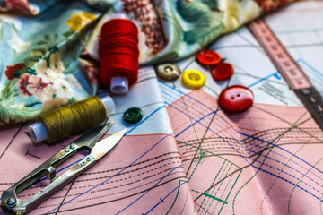 On the cutting table lie scissors, pattern, thread, chalk, fabric, buttons and pins. Work place cutter.