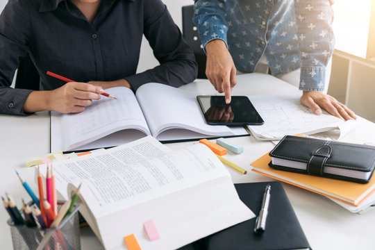 Education, teaching, learning, technology and people concept. Two high school students or classmates with helps friend catching up workbook learning in classroom, Tutor books with friends