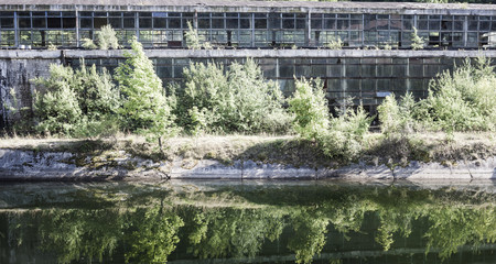 Fototapeta na wymiar Abandoned industrial hall in Romania, outside view, reflected in a river