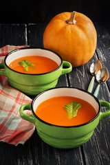 Pumpkin soup puree in ceramic small green saucepans on a wooden table.