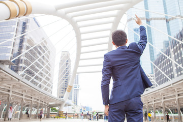 Businessman raising his fist  in the air, with office building background - business success, achievement, and win concepts