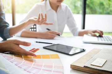 Two young women interior design or graphic designer working on project of architecture drawing with work tools and color swatches, colour chart in digital tablet at workplace