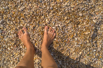 Woman's feet standing on small pebbles and sand. Space for text