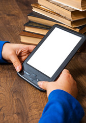 girl's hands hold E-book on mobile device above pile of old paper book  with blank white screen on a wooden background. Concept of teenage life and gadgets
