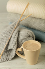 Cup of coffee (cappuccino) and knitting handmade. Pile of knitted clothes blue, white and gray...