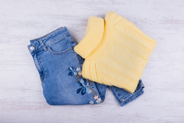 Blue jeans and yellow sweater on white wooden background. Women's fashion clothes.