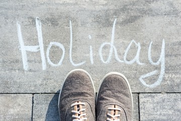 Handwritten word HOLIDAY on the asphalt and sneakers