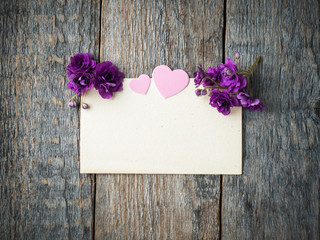 Paper heart and flowers of violets on an old sheet of paper on rustic wooden background
