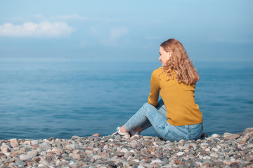 beautiful blonde girl is sitting on the beach and looking at the horizon