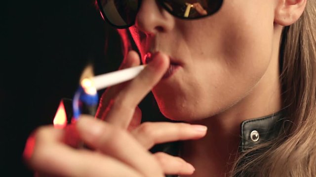 Portrait of elegant blonde woman in glasses smoking a cigarette on black background in studio