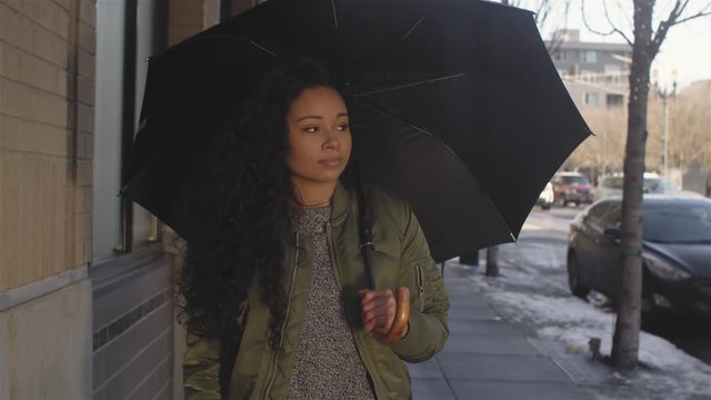 Medium shot of a beautiful young woman walking through the city while holding an umbrella