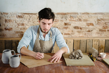 handsome young mexican potter does sketches of ceramics on the paper. concept of small business, handcrafted, hobby work.