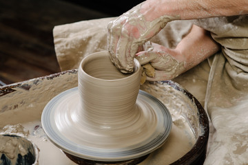 pottery, workshop, ceramics art concept - closeup on male hands sculpt new utensil with a tools and water, man's fingers work with potter wheel and raw fireclay, front close view