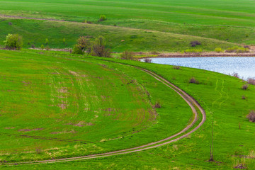 A rural road running along the river bank next to a plowed field. Green spring in Russia.