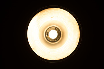 Metalic vintage ceiling lamp closeup. Bright light bulb in round lamp. View from bottom. Vintage image color effect.