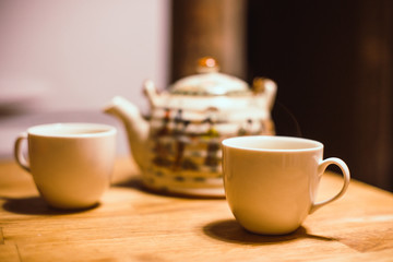 Teapot and 2  white cups with hot tea on  wooden table. Tea drinking time. Vintage image effect.  Natural mood.