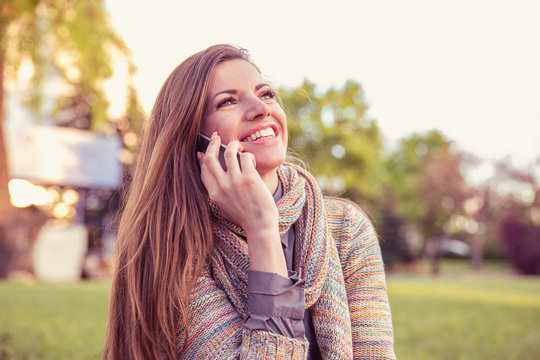 young woman talking on mobile phone. Casual beautiful girl using smartphone smiling happy outside in a park.