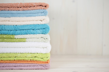 A stack of clean multi-colored towels on a wooden surface.