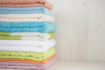 A stack of clean multi-colored towels on a wooden surface.